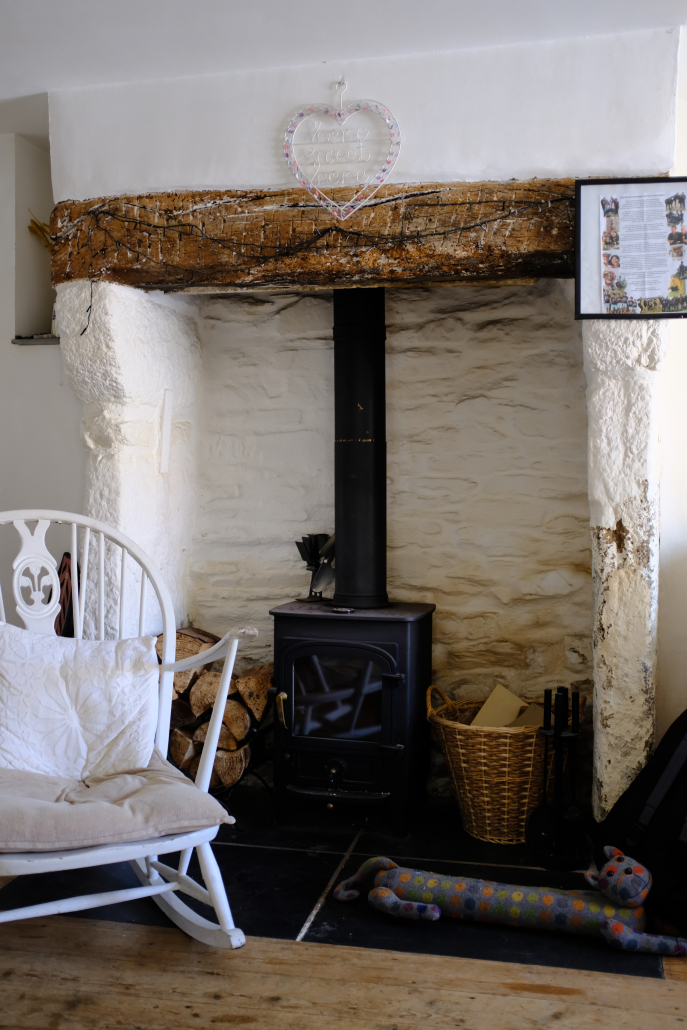 DSCF1873 A white rocking chair sitting in front of a small, black woodburner that's against a white stone wall.