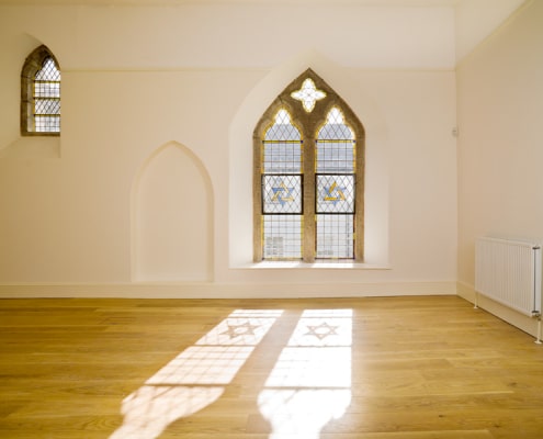 A well-lit, empty room with two windows, a wooden floor and a radiator.