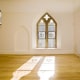 A well-lit, empty room with two windows, a wooden floor and a radiator.