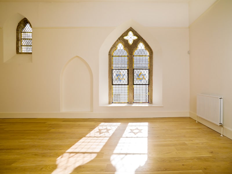 A well-lit, empty room with two windows, a wooden floor and a radiator.